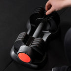 Pair of black dumbbells with red accents on a dark surface, held by a hand.