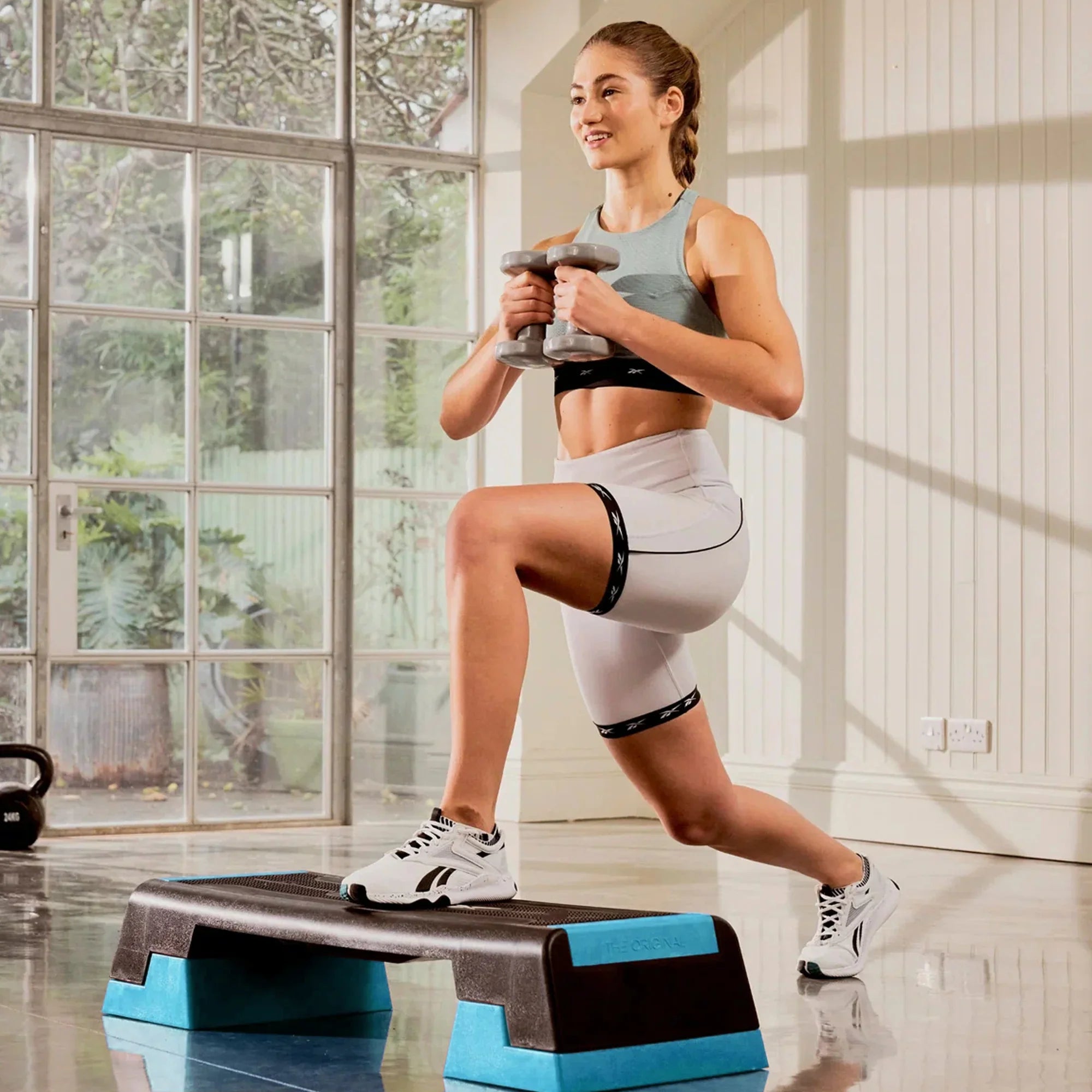 Woman exercising with dumbbells on a step platform in a home setting