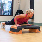 Woman exercising on an orange and black step platform in a gym setting