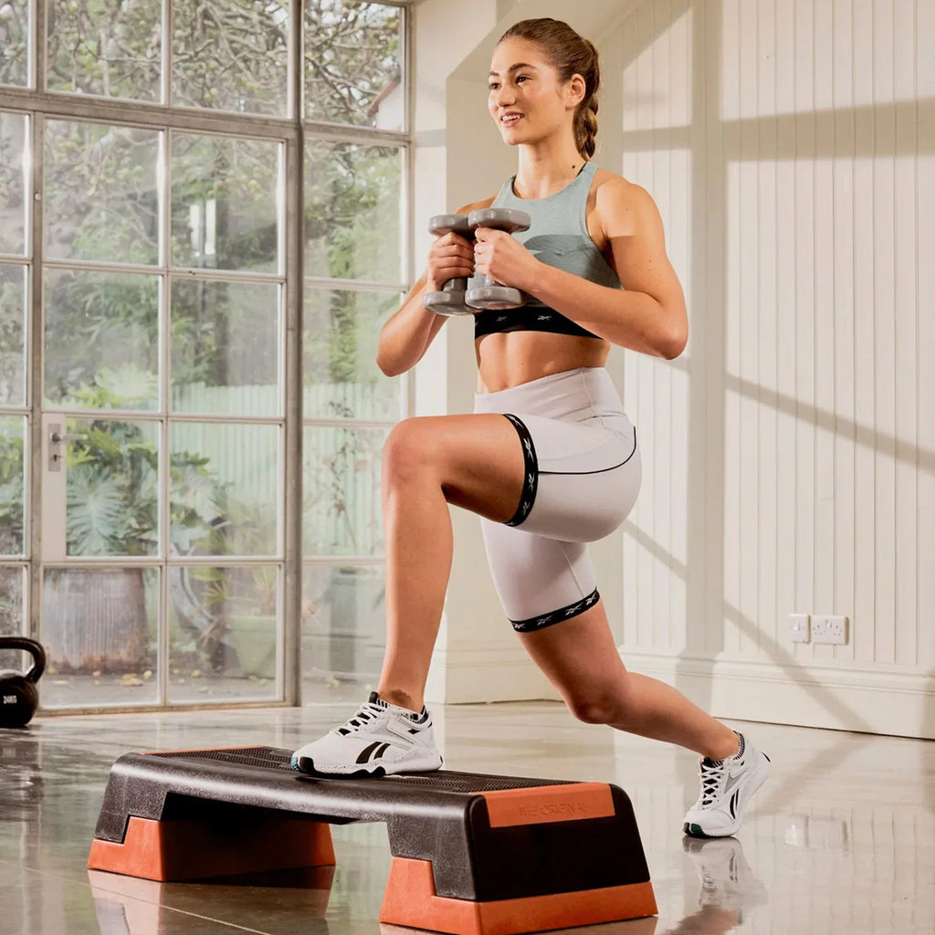Woman exercising with dumbbells on a step platform in a home setting