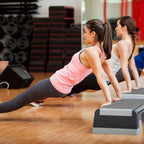 Two women exercising on an step platform in a gym setting