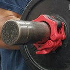 Close-up of a barbell with red clamps being held by a person wearing a blue shirt.