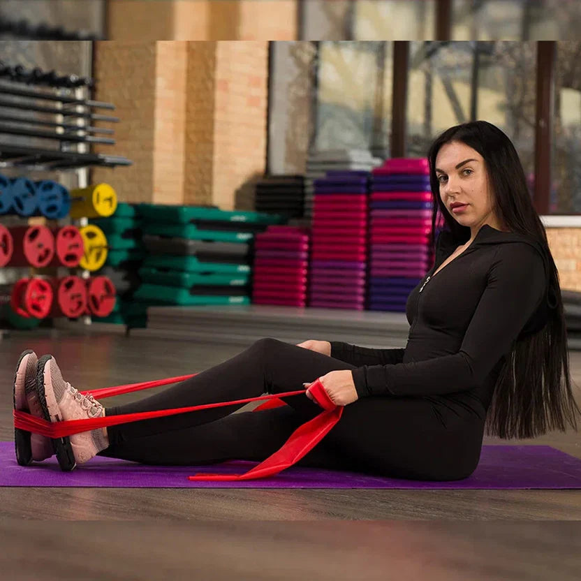 Woman exercising with resistance bands on a purple mat in a gym.