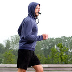 Person wearing a blue hoodie and black shorts running outdoors on a rainy day.